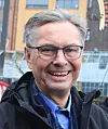 Lächelnder Mann mit Brille vor moderner Gebäude-Fassade im Freien.