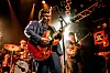 Band spielt auf einer Bühnen mit roter E-Gitarre, Schlagzeug und warmem Konzertlicht.