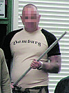 Mann mit „Hamburg“-Shirt hält eine lange Metallstange vor Lamellen im Innenraum.