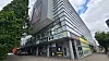 Modernes Gewerbegebäude an Straßenecke mit Glasfassade, Werbeschildern und Bäumen