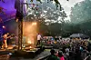 Band auf Open-Air-Bühne vor großem Publikum im Park bei Dämmerung.