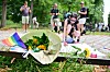 Ashley schreibt vor Blumen und Regenbogenflagge eine Trauerbotschaft am Rand des CSD in Berlin.