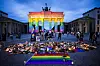 Brandenburger Tor in Regenbogenfarben mit Schriftzug „Berlin, Stadt der Freiheit“, davor Blumen und Kerzen.