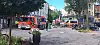 Einsatzfahrzeuge und Absperrungen in einer Innenstadtstraße mit Bäumen und Passanten.