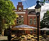 Factory Housebar mit Uhrturm, Sonnenschirmen und leeren Tischen im Biergarten.