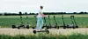 ADAC-Tester fährt E-Scooter auf einem Feldweg, weitere Roller stehen im Hintergrund am Acker.