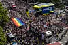Große Menschenmenge in einer Berliner Straße, Regenbogenflagge, Polizeifahrzeuge und Einsatzkräfte sichern die Demo.
