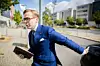 Mann im blauen Anzug steigt aus einem schwarzen Auto vor modernen Gebäuden aus.