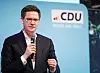 Mann im Anzug spricht mit Mikrofon vor CDU-Hintergrundwand.
