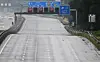 Leere Autobahn mit Fahrbahnmarkierungen, blauen Verkehrsschildern und digitalen Anzeigen an einer Kontrollstelle.