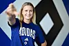 Nikola Karczewska im blauen Adidas-Trikot vor HSV-Logo, lächelt und zeigt auf die Kamera.