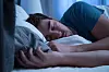 Schlafende Person im Bett, Augen geschlossen, Kopf auf dem Kissen, Hand im Vordergrund.