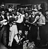 Gruppe von Menschen in einem Innenraum, einige spielen Gitarren und musizieren gemeinsam.