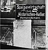 Schaufenster mit der Aufschrift „Speisewirtschaft zum Historischen-Keller Hermann-Homann“ und Auslagen.