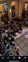 Menschen versammeln sich im Treppenhaus, sitzen auf dem Boden und halten ein großes Protestbanner.