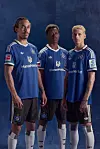 Yussuf Poulsen, Albert Sambi Lokonga und Albert Grønbæk stehen in blauen Trikots vor dunklem Hintergrund