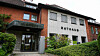 Rathaus mit Backstein- und Putzfassade, Eingang mit Glasvordach und grüner Bepflanzung.