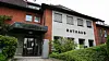 Rathaus mit Backstein- und Putzfassade, Eingang mit Glasvordach und grüner Bepflanzung.
