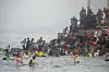 Menschen schwimmen und klettern über die Mole nach Ceuta, Einsatzkräfte stehen am Ufer.