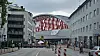 Straßensperrungen leiten den Verkehr vor einer roten Bogenbrücke zwischen Häusern.