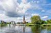 Blick über die Warnow auf Rostocks Altstadtsilhouette mit Kirchturm und Ufergrün.