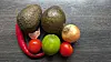 Avocados, Limetten, Tomaten, Zwiebel und rote Chilischote auf dunklem Holz.