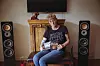 Frau sitzt mit Gitarre zwischen zwei Lautsprechern im Wohnzimmer.