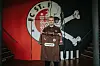 Torhüter im braunen Trikot vor FC-St.-Pauli-Wand mit Logo und Schläger-Silhouette.