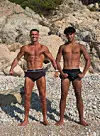 Cristiano Ronaldo und sein Sohn stehen barfuß auf einem Kiesstrand vor Felsen und posieren in Badehosen.