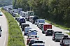 Mehrere Autos und Lkw im dichten Stau auf einer Autobahn, rechts und links von Bäumen und Grünstreifen gesäumt.