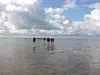 Menschen gehen bei Ebbe über das Watt unter einem wolkigen Himmel.
