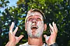 Junger Mann mit Sonnencreme im Gesicht lacht unter freiem Himmel und trägt Creme auf.