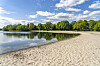 Sandstrand am Eichbaumsee in Allermöhe mit ruhigem Wasser und Uferbäumen.