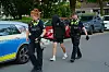 Polizeikräfte führen eine vermummte Person in schwarzer Kleidung an einem Streifenwagen vorbei.