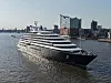 Scenic Eclipse 2 fährt auf ruhigem Wasser vor einer modernen Stadtsilhouette.