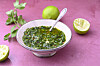 Kräuter-Chimichurri in einer Schale mit Limette, daneben Limettenhälften und Kräuter.