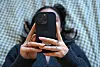 Person hält Smartphone vor das Gesicht, im Hintergrund unscharf mit KI-Hinweis im Social-Media-Kontext.