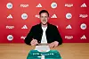 Mann an Tisch mit grün-weißem Trikot vor roter Wand mit Ziggo- und Adidas-Logos.