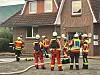 Feuerwehrkräfte stehen mit Schläuchen vor einem Wohnhaus mit rotem Ziegeldach.
