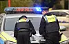 Zwei Polizisten prüfen an einem Streifenwagen einen Unfallort mit Blaulicht.