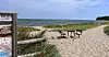 Sandweg durch Dünen zu Tisch und Stühlen am Strand vor dem Meer.