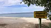 Gelbes Schild „Unbewachte Badestelle“ an einem leeren Strand mit Meer im Hintergrund.