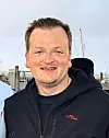 Mann in schwarzem Hoodie vor Hafen mit Masten und Booten.