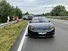 Porsche mit Totalschaden steht auf der Landstraße, Einsatzkräfte sichern die Unfallstelle.