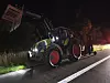 Traktor am Straßenrand bei Nacht mit eingeschaltetem Licht, dahinter eine Person in roter Kleidung.