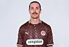 Jackson Irvine steht im braunen FC-St.-Pauli-Trikot vor hellem Hintergrund.
