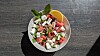 Bunter Salat mit Tomaten, Gurke, Feta und Kräutern in einer Schüssel auf dunklem Tisch.