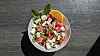 Bunter Salat mit Tomaten, Gurke, Feta und Kräutern in einer Schüssel auf dunklem Tisch.