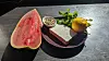 Wassermelone, Käse, Kräuter und Zitrone auf einem dunklen Teller im Sonnenlicht
