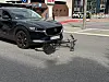 Schwarzer Mazda zieht einen beschädigten Fahrradanhänger auf einer Straße in der Stadt.